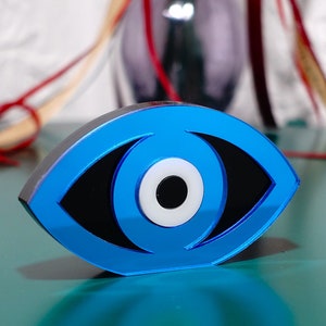 Op de afbeelding: Een blauwe boze oog-amulet met een wit centrum en een zwarte pupil. De amulet is gemaakt van glas en heeft een glanzende afwerking.
