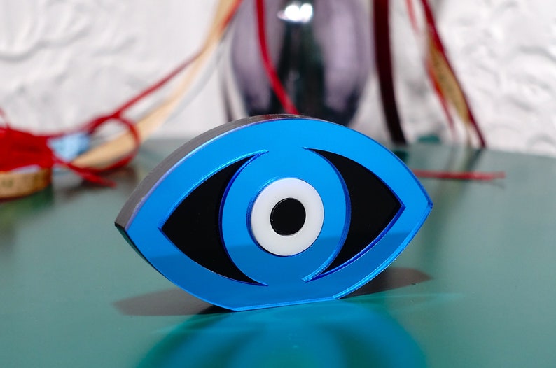 Op de afbeelding: Een blauwe boze oog-amulet met een wit centrum en een zwarte pupil. De amulet is gemaakt van glas en heeft een glanzende afwerking.