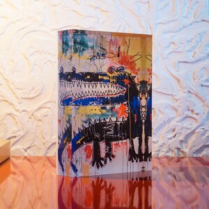 Puede incluir: Un bloque acr&iacute;lico colorido con una pintura abstracta de un cocodrilo en negro y azul. La pintura est&aacute; sobre un fondo blanco con salpicaduras de pintura amarilla, roja y naranja.