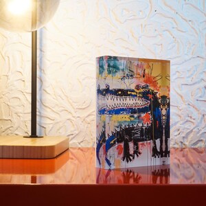 Puede incluir: Un bloque acr&iacute;lico colorido con una ilustraci&oacute;n de un cocodrilo negro y azul. El cocodrilo tiene una boca grande con dientes afilados y est&aacute; rodeado de formas y l&iacute;neas abstractas de colores.