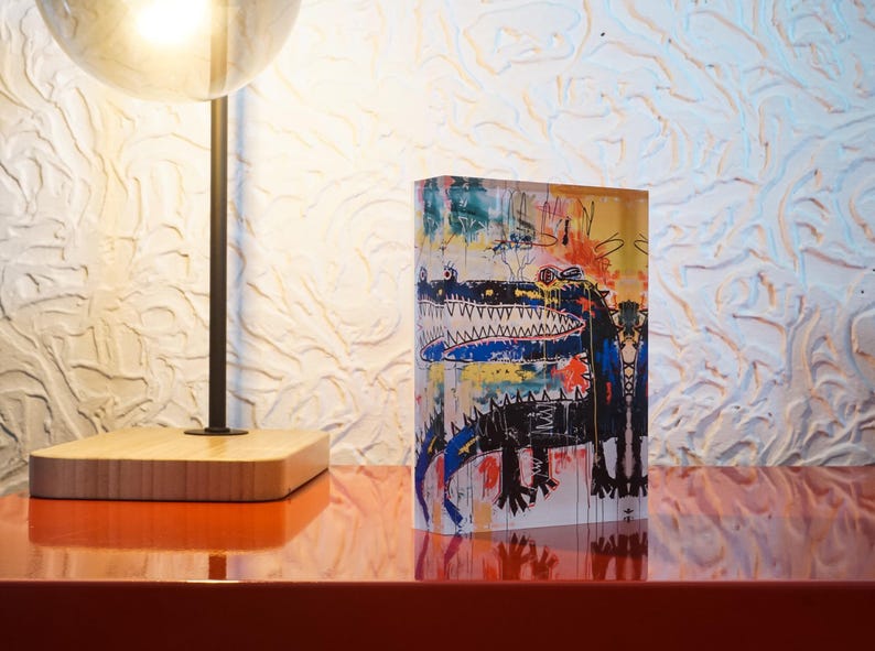 Puede incluir: Un bloque acr&iacute;lico colorido con una ilustraci&oacute;n de un cocodrilo negro y azul. El cocodrilo tiene una boca grande con dientes afilados y est&aacute; rodeado de formas y l&iacute;neas abstractas de colores.