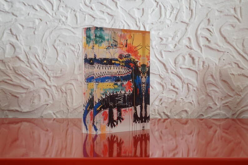 Puede incluir: Una pintura acr&iacute;lica abstracta colorida sobre un bloque de acr&iacute;lico transparente. La pintura presenta un caim&aacute;n negro y azul con una gran boca abierta y dientes blancos. El fondo es una mezcla de amarillo, naranja, azul y verde.