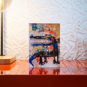 Puede incluir: Una pintura abstracta colorida de un cocodrilo con un cuerpo azul y negro sobre un fondo blanco. La pintura est&aacute; enmarcada y colgada en una pared.