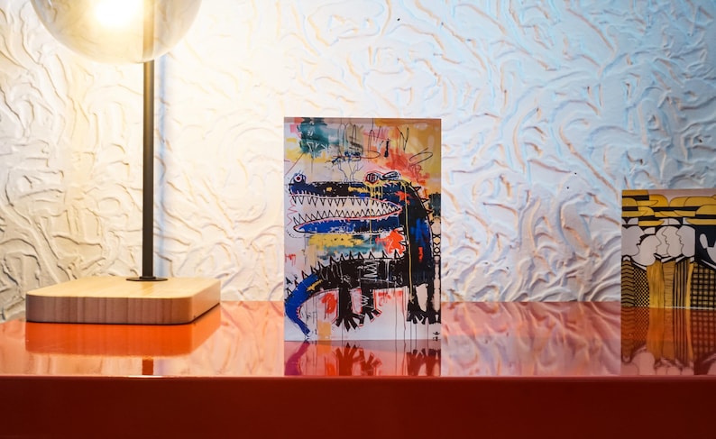 Puede incluir: Una pintura abstracta colorida de un cocodrilo con un cuerpo azul y negro sobre un fondo blanco. La pintura est&aacute; enmarcada y colgada en una pared.