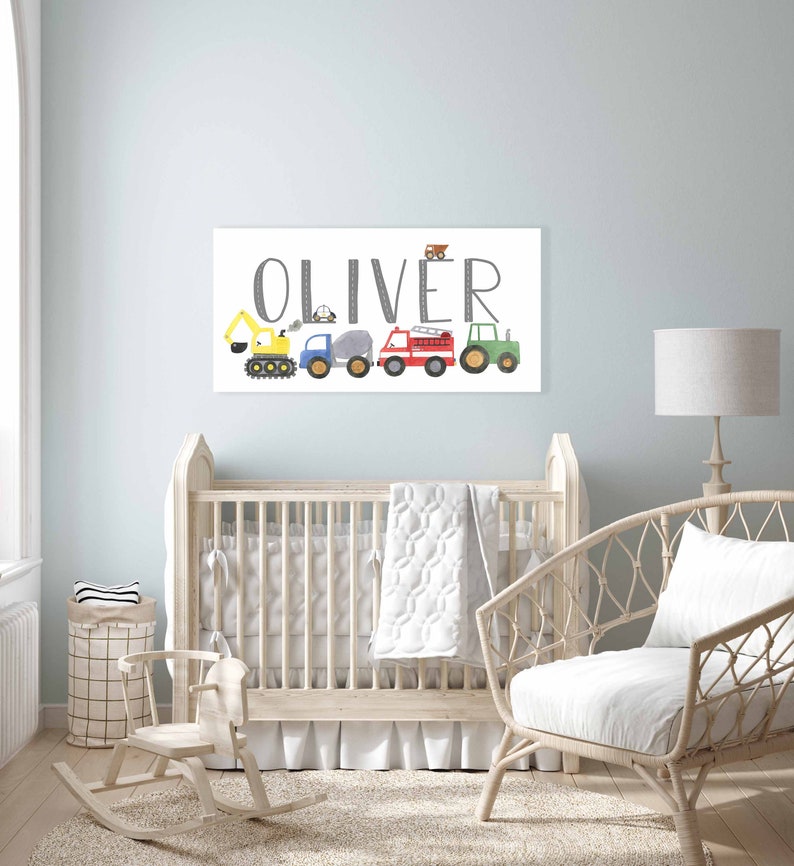 K&ouml;nnte beinhalten: Ein wei&szlig;er Leinwanddruck mit dem Namen "Oliver" in grauer Schrift. Der Name ist mit einer Reihe von bunten Spielzeugfahrzeugen verziert, darunter ein gelber Bagger, ein blauer LKW, ein grauer Betonmischer, ein rotes Feuerwehrauto und ein gr&uuml;ner Traktor.