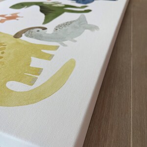 Pode incluir: Uma impress&atilde;o em tela branca com uma pintura em aquarela de uma linha de dinossauros. Os dinossauros s&atilde;o de v&aacute;rias cores, incluindo amarelo, verde, azul e laranja. Os dinossauros est&atilde;o olhando para o lado direito da imagem.