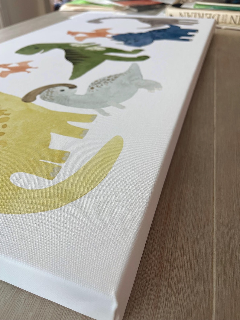Pode incluir: Uma impress&atilde;o em tela branca com uma pintura em aquarela de uma linha de dinossauros. Os dinossauros s&atilde;o de v&aacute;rias cores, incluindo amarelo, verde, azul e laranja. Os dinossauros est&atilde;o olhando para o lado direito da imagem.