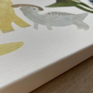 Pode incluir: Um close-up da borda de uma tela branca com uma superf&iacute;cie texturizada. A tela tem uma pintura de um dinossauro amarelo, um dinossauro verde e um dinossauro cinza com manchas marrons.