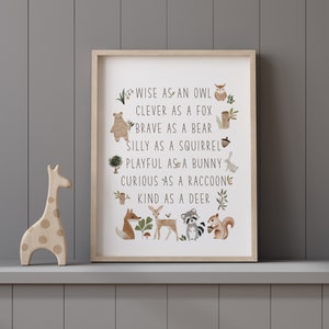 May include: A framed print with a white background and brown text that reads "WISE AS AN OWL, CLEVER AS A FOX, BRAVE AS A BEAR, SILLY AS A SQUIRREL, PLAYFUL AS A BUNNY, CURIOUS AS A RACCOON, KIND AS A DEER". The text is surrounded by illustrations of animals, including an owl, fox, bear, squirrel, bunny, raccoon, and deer.