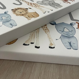 May include: A white canvas with the name "Justin" printed in gray letters. The canvas features a line of watercolor animal illustrations, including a rhinoceros, a lion, a giraffe, an elephant, and a tiger.