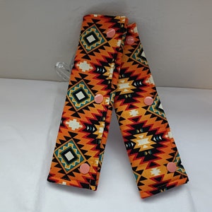 May include: Two orange, black and white patterned fabric straps with pink buttons. The straps are designed to be used as stroller straps.