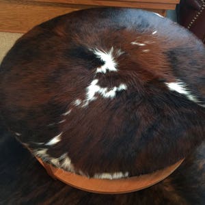 May include: A round brown and white cowhide ottoman with a wooden base.