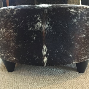 May include: A round, black and white cowhide ottoman with short, black legs.