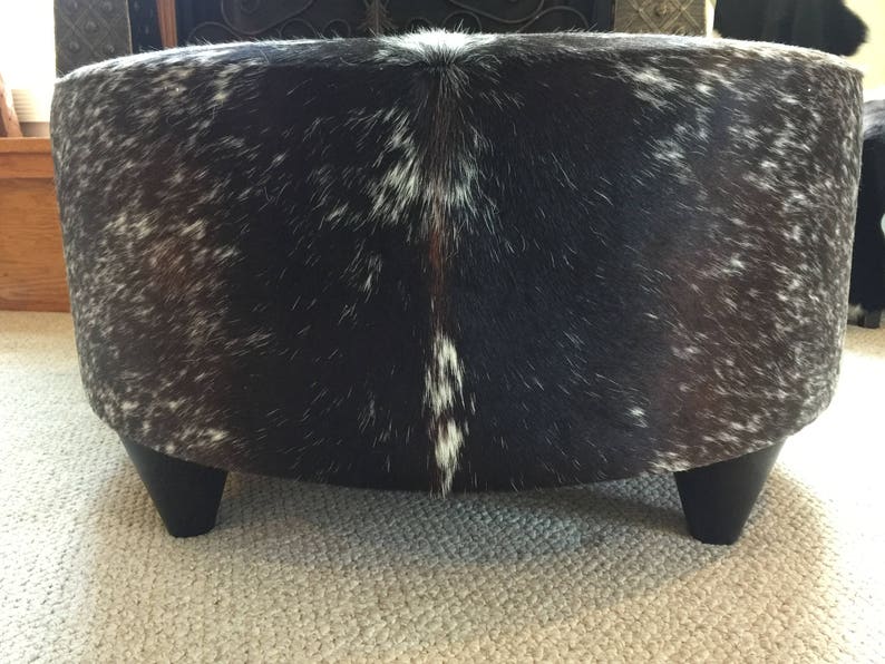 May include: A round, black and white cowhide ottoman with short, black legs.