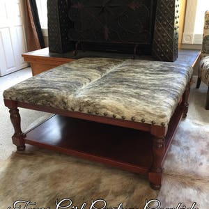 May include: A brown wooden coffee table with a cowhide top and a lower shelf. The table is sitting on a cowhide rug. The text "Texas Girl Custom Cowhide" is visible in the bottom right corner of the image.
