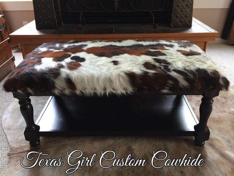 May include: A black wooden coffee table with a cowhide top. The table has a lower shelf and turned legs.