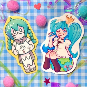 May include: Two cartoon character stickers. The first sticker is of a girl with green hair and glasses holding a white cat. The second sticker is of a girl with blue hair wearing a crown and a white dress sitting on a green globe.