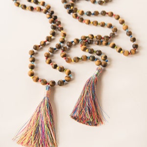 May include: A brown tiger's eye beaded necklace with colorful accents and two multi-colored tassels.