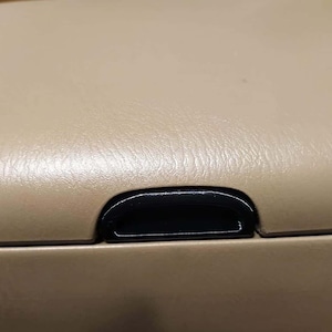 Puede incluir: Primer plano del interior beige de un coche con una manija de plástico negro.