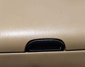 Puede incluir: Primer plano del interior beige de un coche con una manija de plástico negro.