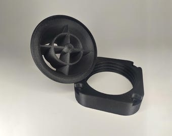 Puede incluir: Un objeto de plástico negro impreso en 3D con una parte superior circular y una base cuadrada. La parte superior tiene un diseño en forma de estrella de cuatro puntas.