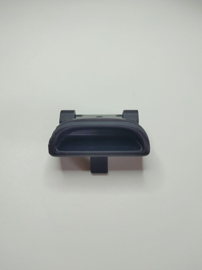 Puede incluir: Una manija de puerta de pl&aacute;stico negro con una abertura rectangular. La manija tiene un peque&ntilde;o pomo redondo en la parte superior.