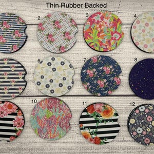 May include: A collection of twelve round car coasters with various floral and patterned designs. The coasters feature a thin rubber backing and include designs with stripes, polka dots, and floral arrangements in shades of pink, blue, and yellow.