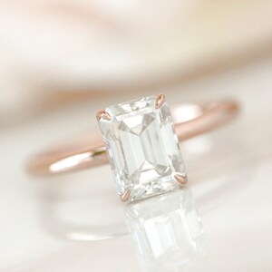May include: A rose gold engagement ring with a large, clear emerald cut diamond.