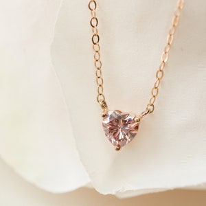 Puede incluir: Un delicado collar de cadena dorada con un colgante de coraz&oacute;n de piedra preciosa rosa.