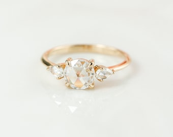 May include: A gold ring with a large oval-shaped diamond and two smaller pear-shaped diamonds on either side.