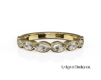 May include: A gold band ring featuring a series of marquise-cut diamonds. The diamonds are set in a bezel style, creating a continuous row of sparkling gemstones. The ring has a polished finish and a classic design.