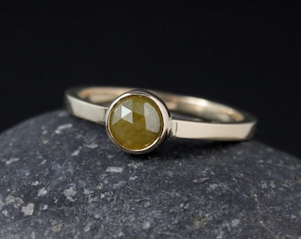 May include: A gold ring with a round, bezel-set, yellow diamond.