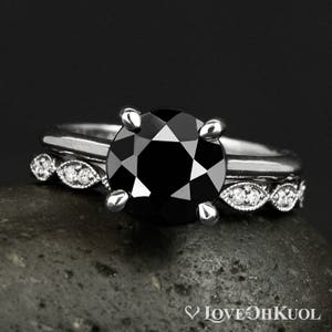 May include: A black diamond engagement ring with a silver band and a matching silver band with small diamonds. The ring is set on a gray stone.