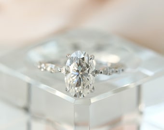 May include: A silver ring with a large oval-shaped diamond set in a prong setting. The band is decorated with smaller diamonds.