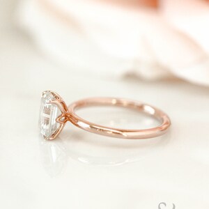 May include: A rose gold engagement ring with a clear, emerald-cut gemstone.