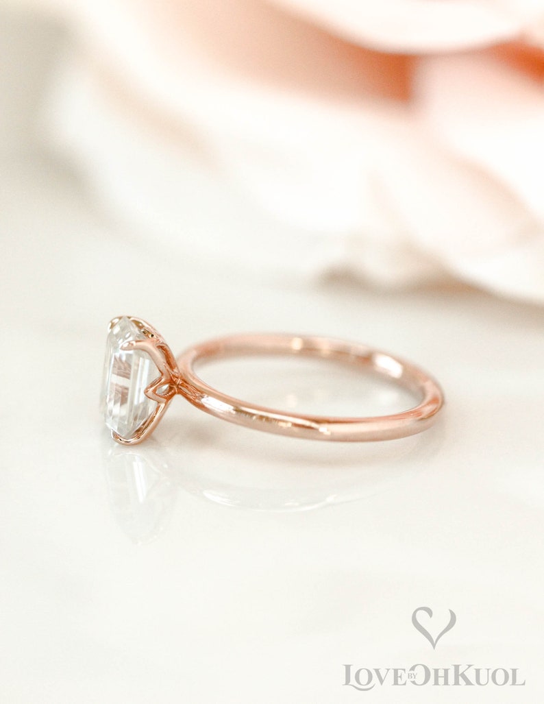 May include: A rose gold engagement ring with a clear, emerald-cut gemstone.