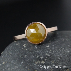 Puede incluir: Un anillo de oro rosa con una piedra preciosa redonda, amarilla y facetada engastada en un engaste de bisel.