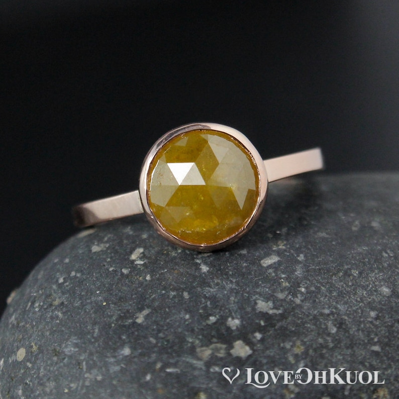 Puede incluir: Un anillo de oro rosa con una piedra preciosa redonda, amarilla y facetada engastada en un engaste de bisel.