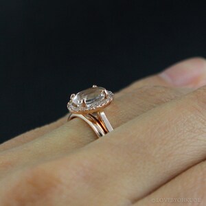 May include: A rose gold engagement ring with a large oval-shaped center stone surrounded by a halo of smaller diamonds. The ring is worn on a person's finger.