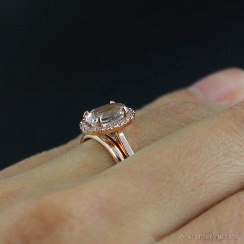 May include: A rose gold engagement ring with a large oval-shaped center stone surrounded by a halo of smaller diamonds. The ring is worn on a person's finger.