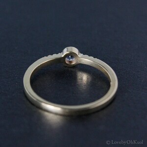 May include: A gold band ring with a single round gemstone set in the center. The band is accented with small gemstones.