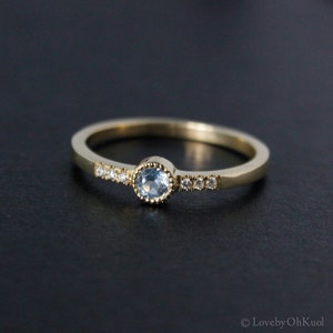 May include: A delicate gold ring with a light blue gemstone surrounded by smaller clear gemstones.