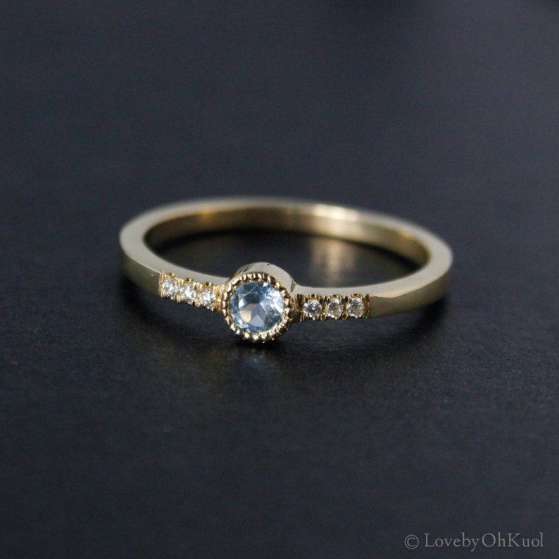 May include: A delicate gold ring with a light blue gemstone surrounded by smaller clear gemstones.