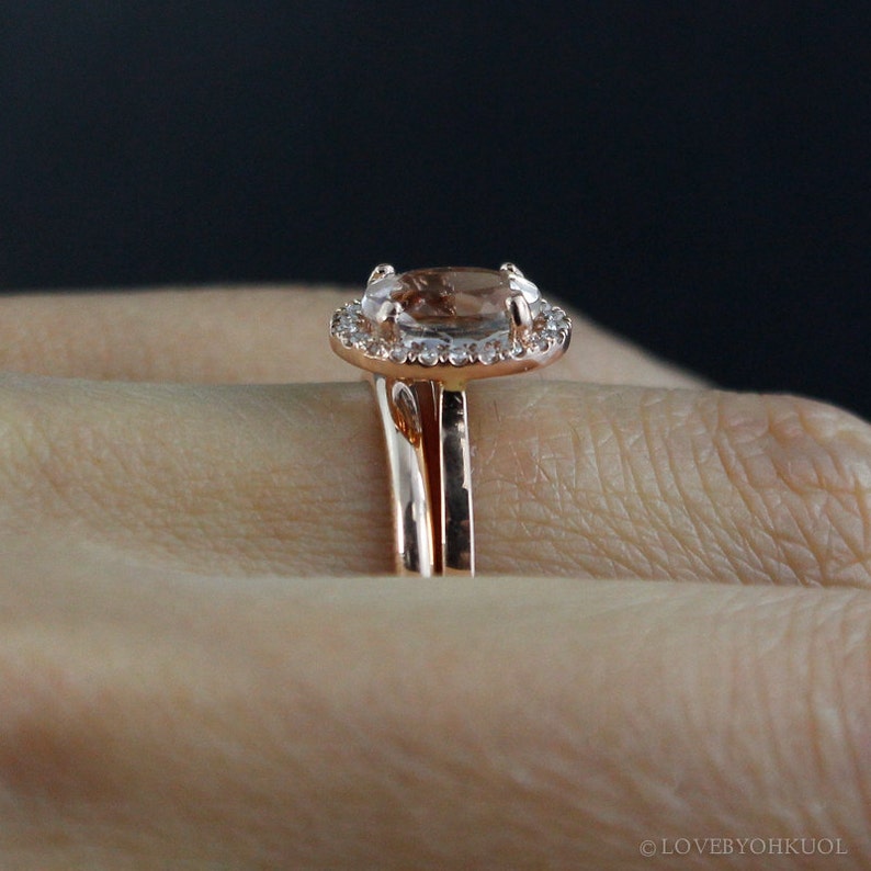 May include: A rose gold engagement ring set with a large oval-shaped center stone surrounded by a halo of smaller stones. The ring is worn on a finger.