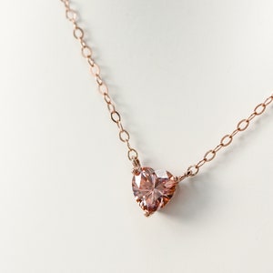 Puede incluir: Un delicado collar de cadena de oro rosa con un colgante de piedra preciosa rosa en forma de coraz&oacute;n.