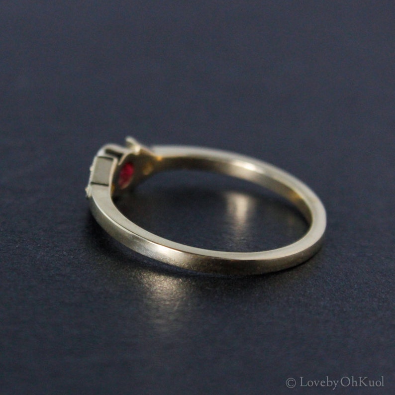 May include: A gold band ring with a single red gemstone set in the center. The ring is simple and elegant.