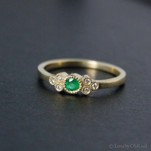 Pu&ograve; includere: Un anello d'oro con uno smeraldo verde circondato da diamanti pi&ugrave; piccoli.