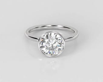 May include: A silver ring with a bezel setting featuring a round, clear diamond.