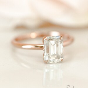 May include: A rose gold engagement ring with an emerald cut diamond.