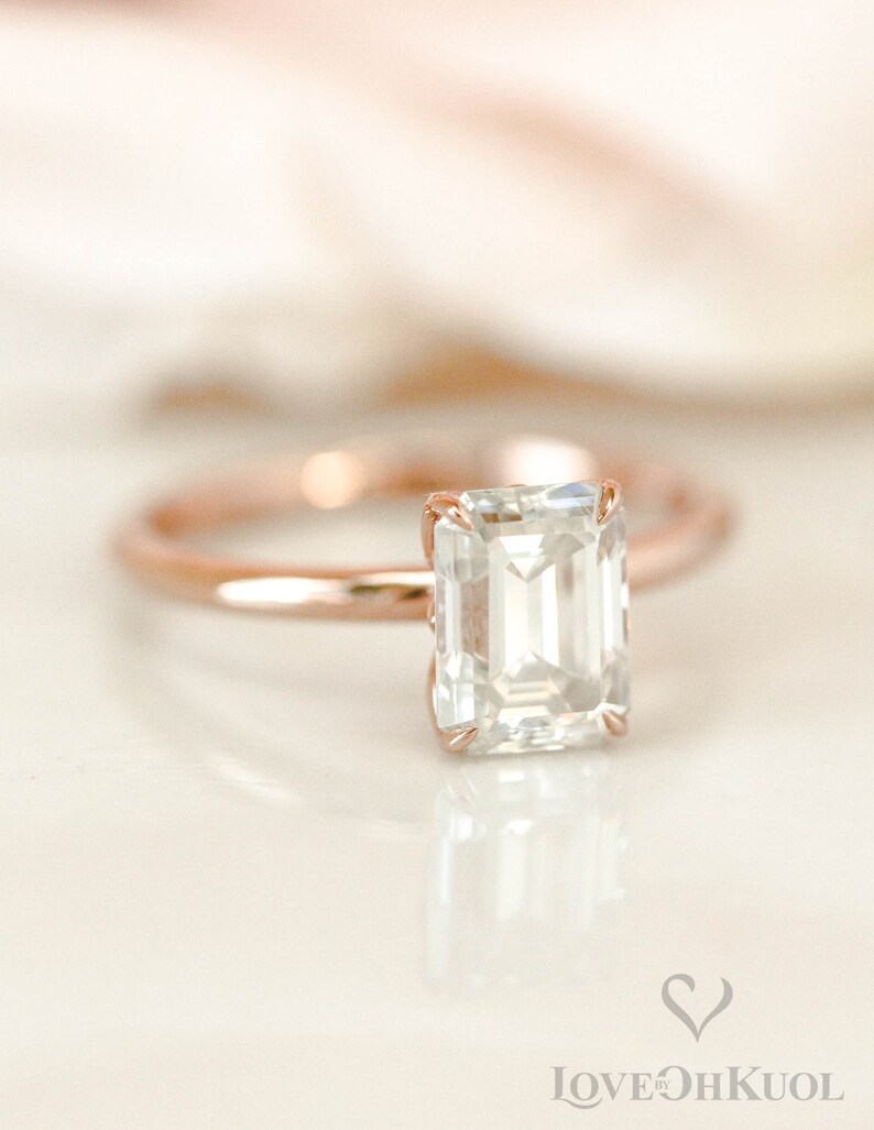 May include: A rose gold engagement ring with an emerald cut diamond.